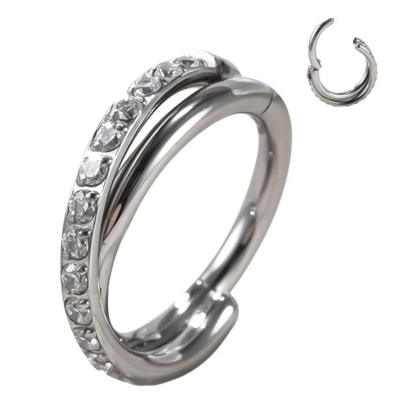 Clicker ring con intreccio doppio cz stone. Questo piercing realizzato in titanio ASTM F136 da implantologia certificato. E' dotato di cerniera, che rende la chiusura molto semplice: basta tirare il segmento per aprirlo, inserire il gioiello nel piercing e chiuderlo con un click. La parte frontale presenta una doppia fila con una serie di scintillanti pietre che ti faranno splendere.